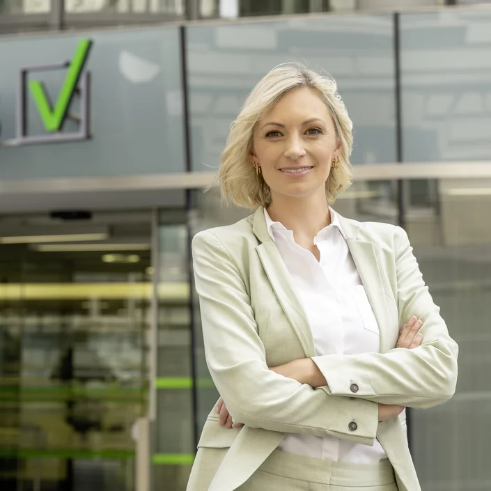 Eine weibliche Person mit blonden Haaren und hellem Hosenanzug vor dem VKB-Kompetenzzentrum in Linz